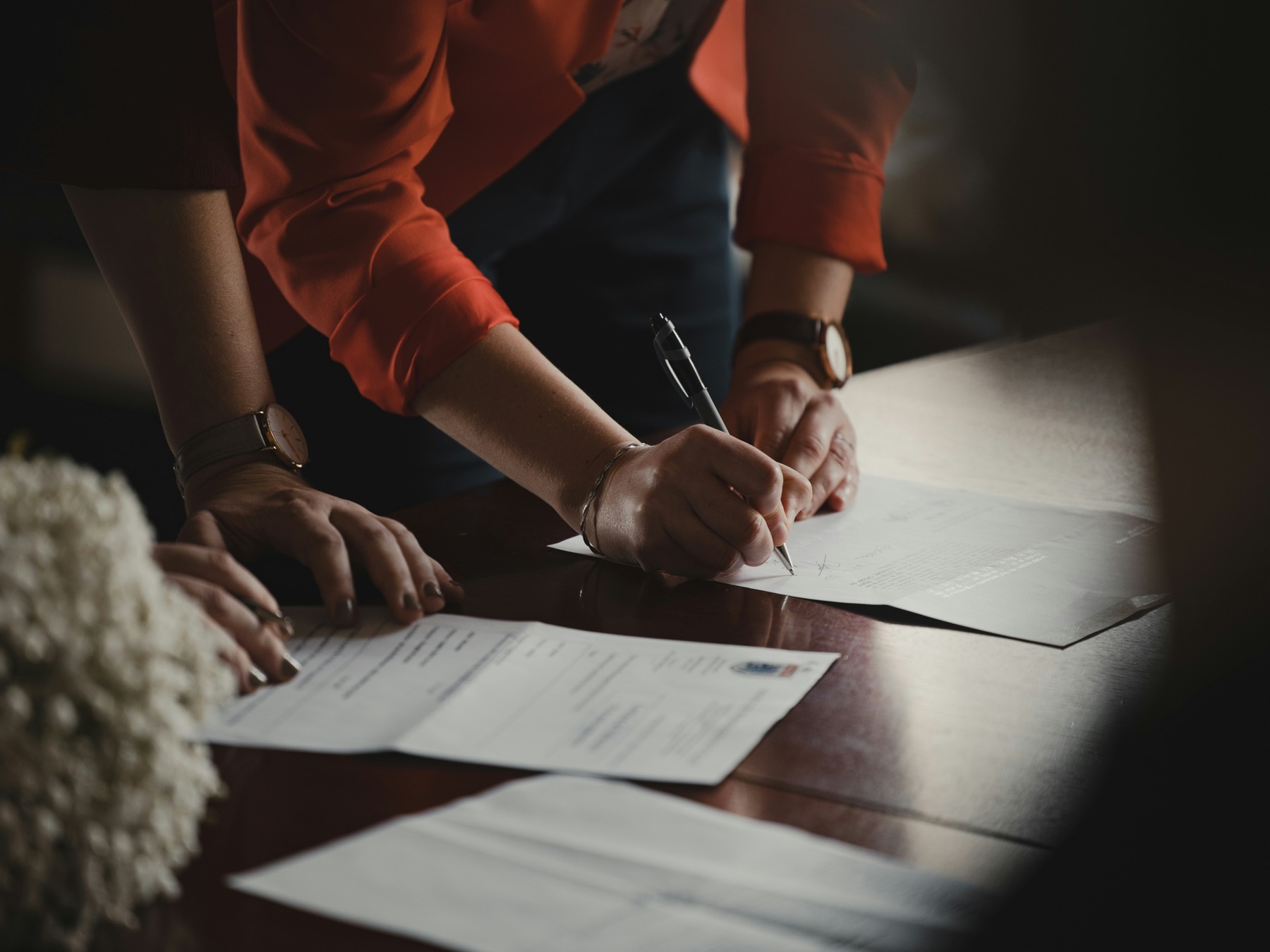 Two people signing a contract at a desk, rendered in deep shadow